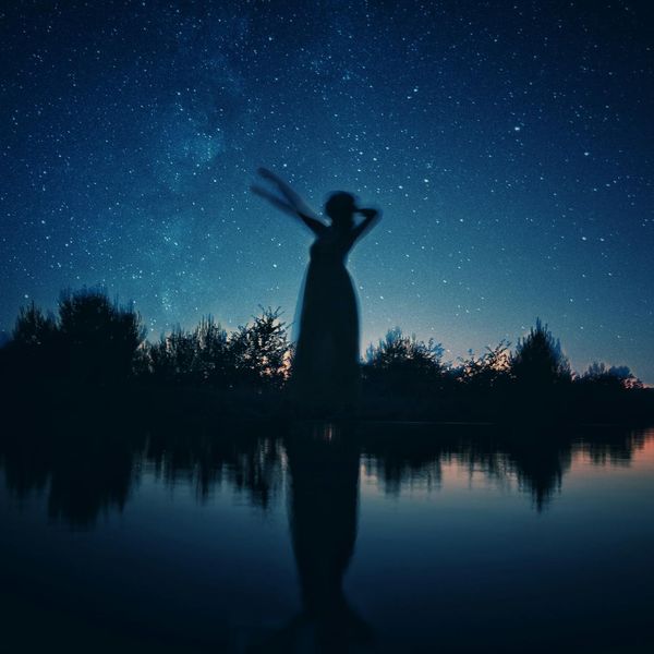 Person peacefully meditating outdoors near a tranquil lake.